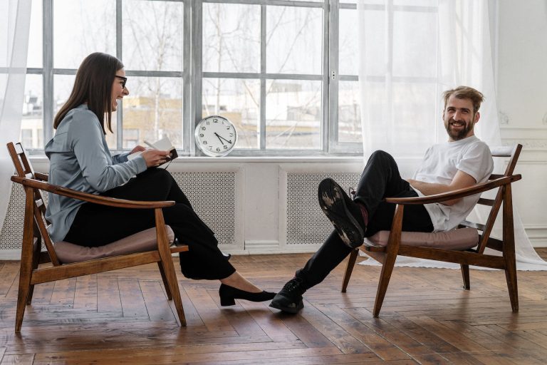Two people sit in a beautifully lit room with many windows doing coaching and training.