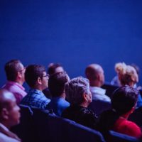 A crowd of people fill a lecture hall during a conference keynote presentation.