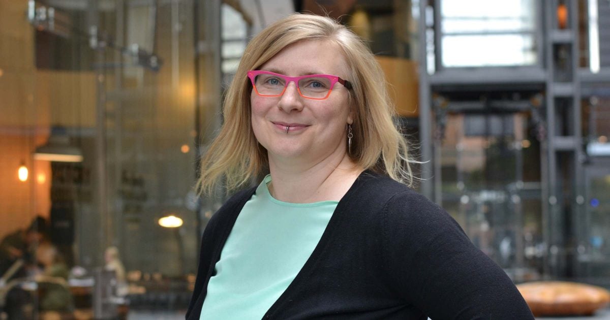 Rebecca Cory: a white woman in her thirties wears a black cardigan over a mint blouse and wears her pink and orang glasses.