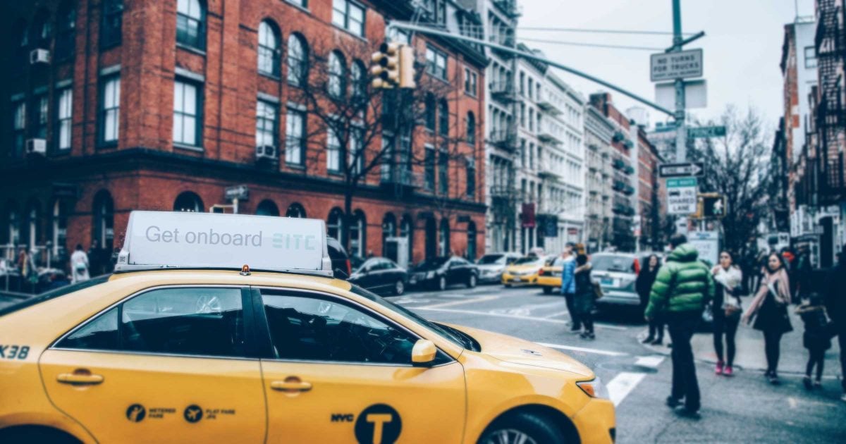 A taxi waits at a busy intersection for someone to get in: "get onboard"