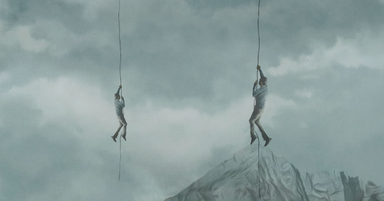 Two people hang from ropes in the clouds, but one of them has their toes resting on the tip of a large rock.