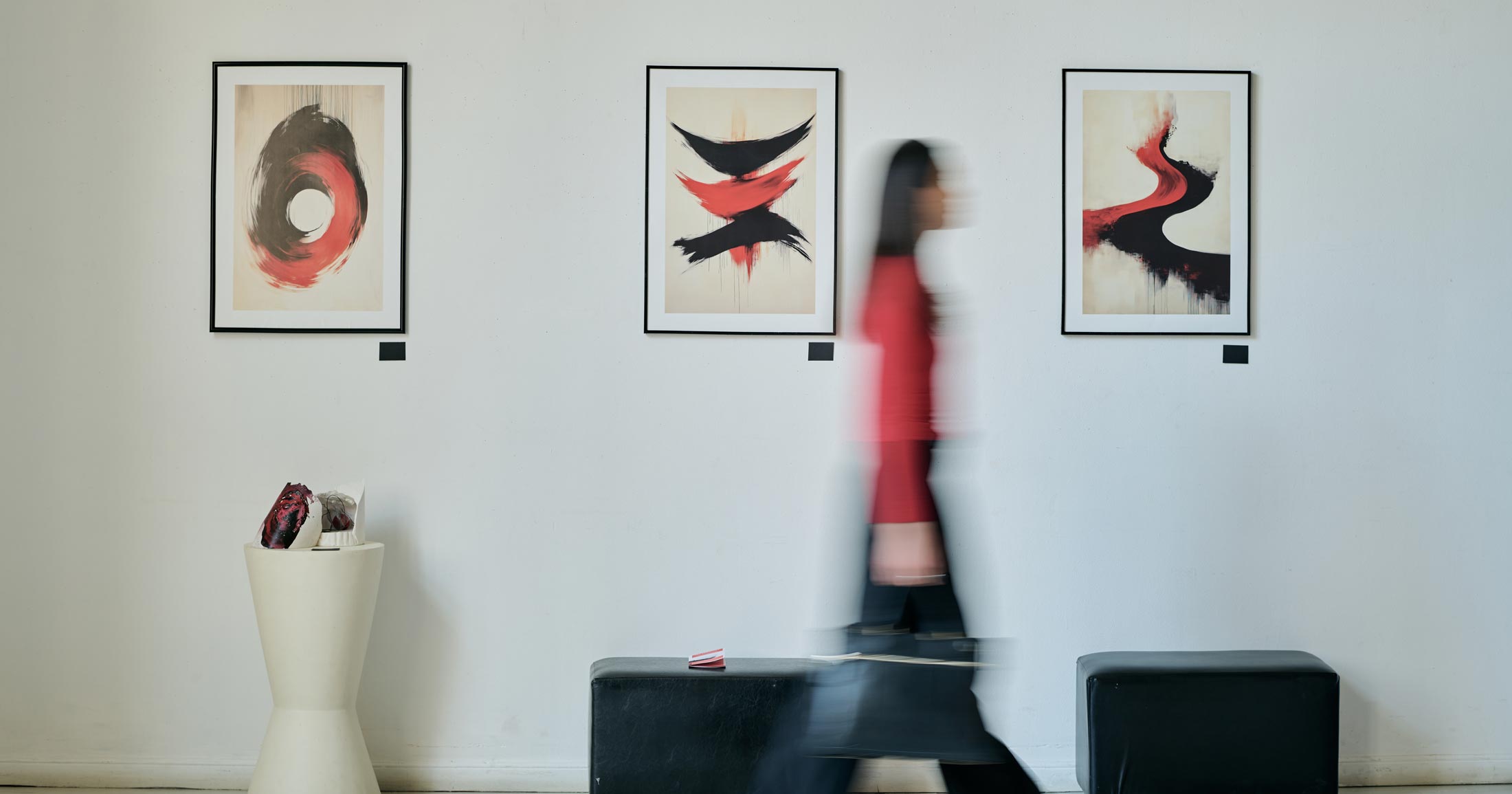 A woman walks past some art, in a blur, her red and black pants are only visible as a blur.